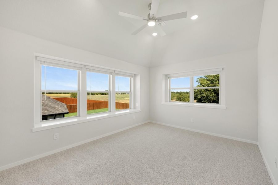 Empty bedroom with vaulted ceiling, ceiling fan, carpet flooring, and multiple windows with outdoor views