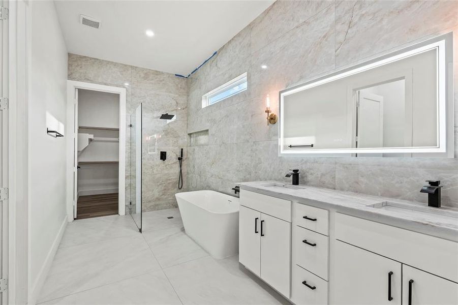 Full bathroom with walk in shower, a freestanding bath, tile walls, double vanity, and light tile patterned floors