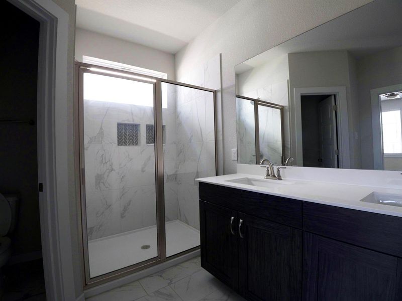 Bathroom featuring light marble finish flooring, a marble finish shower, and double vanity Bathroom featuring light marble finish flooring, a marble finish shower, and double vanity
