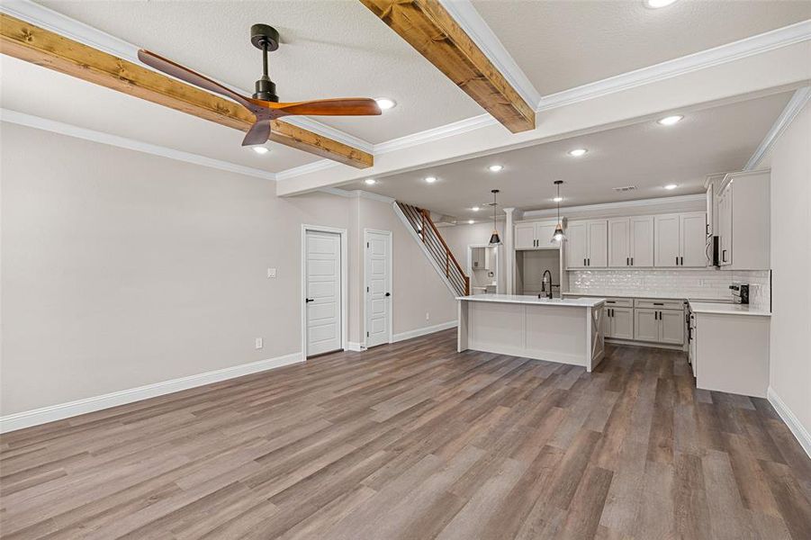 Kitchen featuring hardwood / wood-style floors, beam ceiling, a kitchen island with sink, ceiling fan, and hanging light fixtures