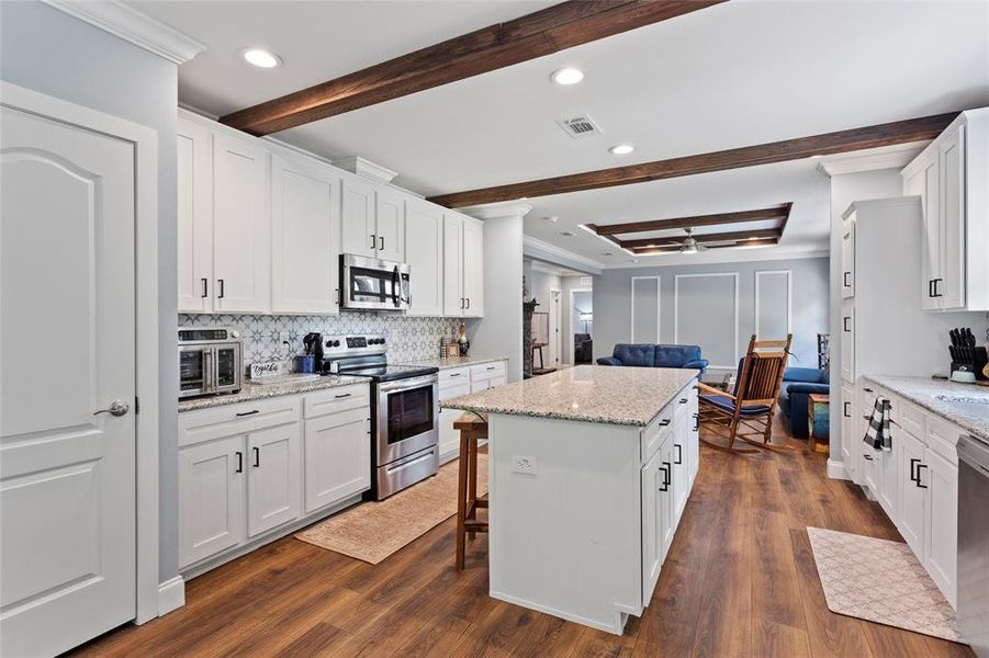 Looking back into the kitchen from the Dining Room, you see the ceiling beams for aesthetics, great kitchen design, and a view of all the cabinets for all your storage needs.  Plus there is great counter space for all of your prepping needs