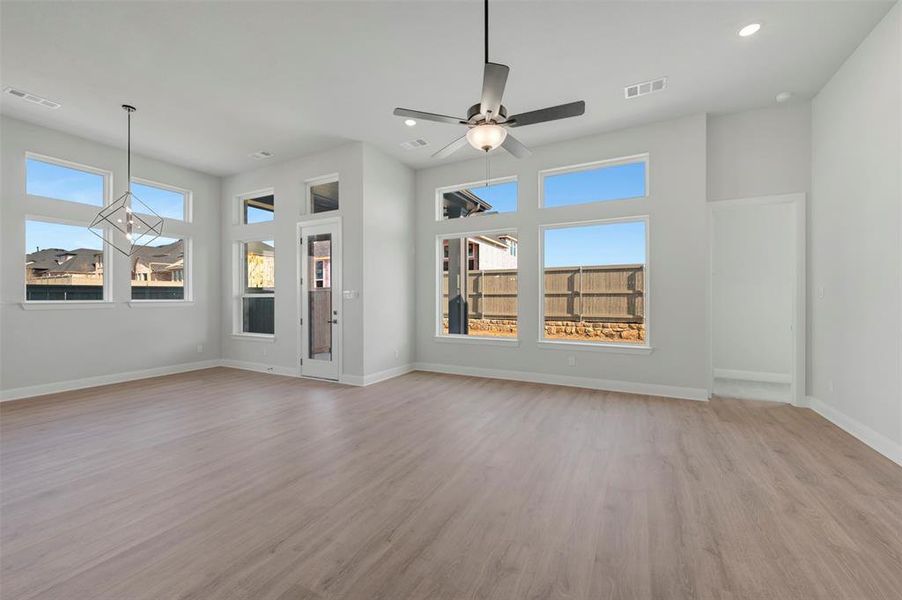 Unfurnished living room featuring light wood-type flooring, ceiling fan, healthy amount of natural light, recessed lighting, and a high ceiling