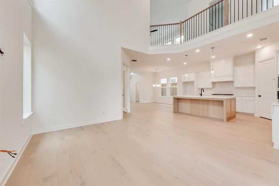 Unfurnished living room featuring a high ceiling, light wood-style flooring, and recessed lighting Unfurnished living room featuring a high ceiling, light wood-style flooring, and recessed lighting