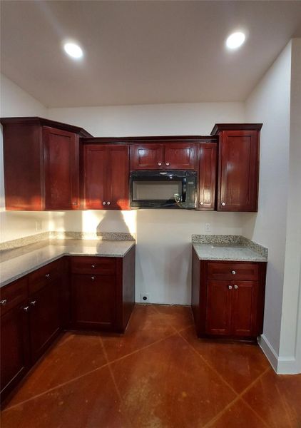 Kitchen featuring bold wood finish cabinetry, black microwave, light stone counters, and recessed lighting