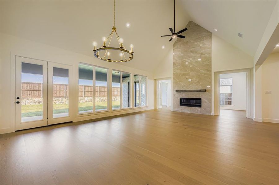 Unfurnished living room with high vaulted ceiling, light wood-style floors, a chandelier, a high end fireplace, and a ceiling fan