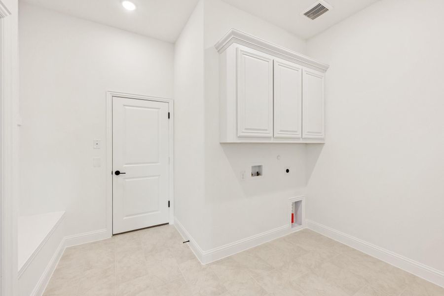 Laundry room with white upper cabinets, washer and dryer hookups, and light tile flooring