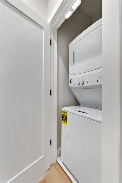 Dedicated laundry closet featuring a white stackable washer and dryer unit, overhead lighting, and light hardwood flooring Dedicated laundry closet featuring a white stackable washer and dryer unit, overhead lighting, and light hardwood flooring