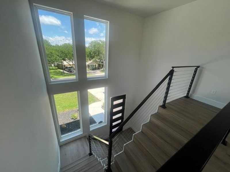 Two-story entry featuring a modern wood-finish staircase with cable railing, white walls, and multiple rectangular windows Two-story entry featuring a modern wood-finish staircase with cable railing, white walls, and multiple rectangular windows