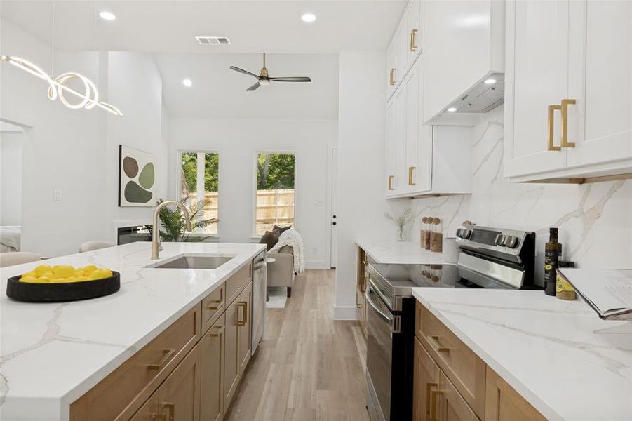 Modern kitchen featuring a large island with an undermount sink and gold-finish faucet, white cabinetry with gold-finish hardware, stainless steel appliances, and wood-finish flooring Modern kitchen featuring a large island with an undermount sink and gold-finish faucet, white cabinetry with gold-finish hardware, stainless steel appliances, and wood-finish flooring