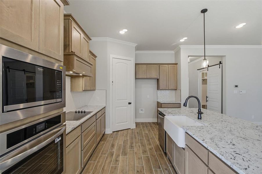 Kitchen with stainless steel appliances, wood finish floors, light stone counters, a barn door, and hanging light fixtures
