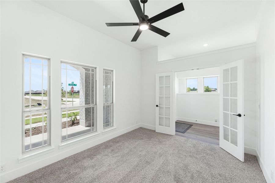 Empty bedroom with gray carpet, black ceiling fan, and white French doors