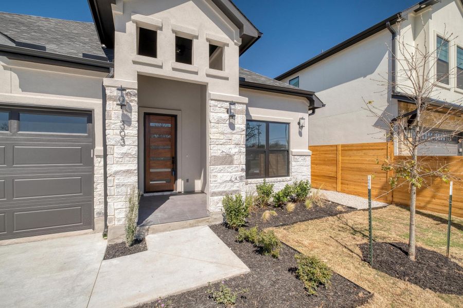 Property entrance featuring stucco siding, stone siding, a garage, and fence