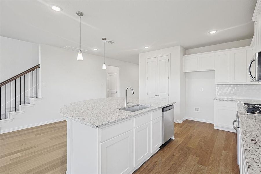 Kitchen featuring light stone counters, light hardwood / wood-style flooring, a kitchen island with sink, and sink