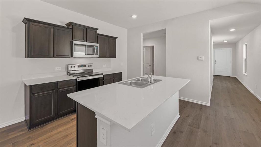 Kitchen featuring dark wood-finish cabinetry, stainless steel appliances, and a central island with an integrated double sink