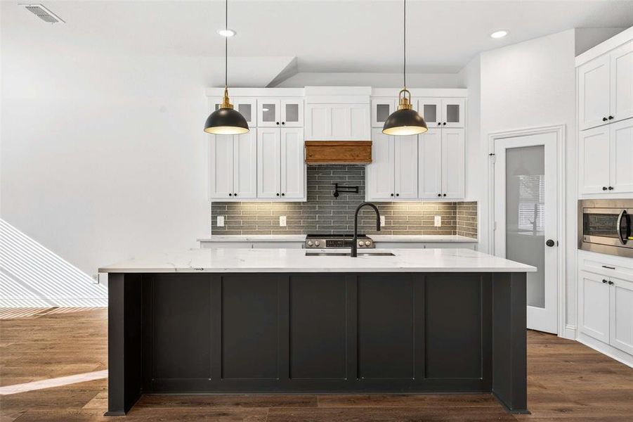 Kitchen featuring decorative light fixtures, an island with sink, decorative backsplash, white cabinetry, and recessed lighting