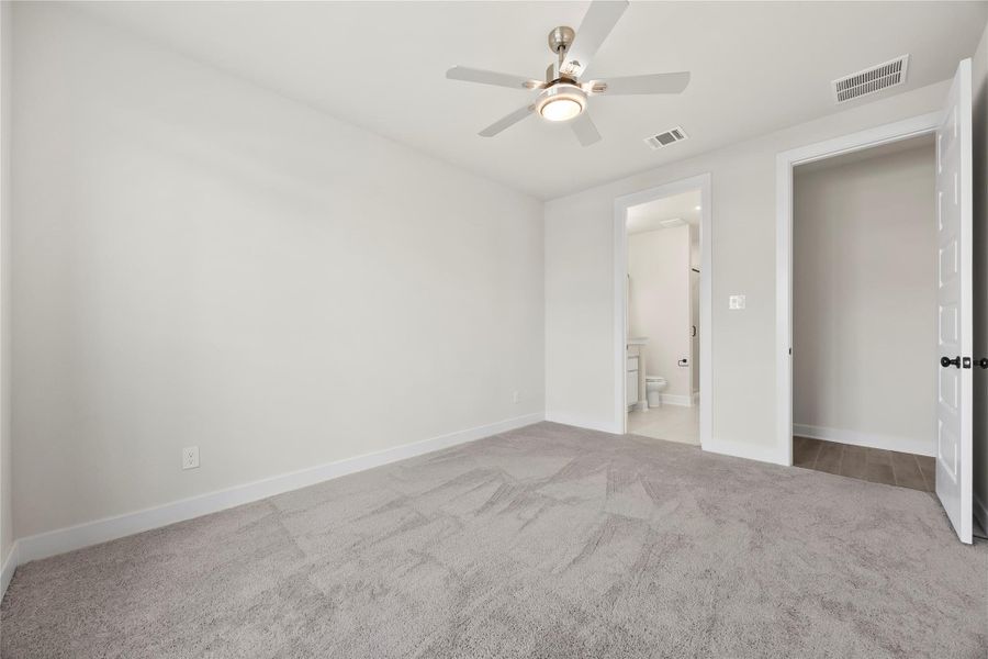This photo shows a bright, unfurnished room downstairs with neutral carpeting and walls, featuring a ceiling fan and recessed lighting. There's an open doorway leading to a bathroom and another to a hallway or closet, providing a clean and versatile space. This photo shows a bright, unfurnished room downstairs with neutral carpeting and walls, featuring a ceiling fan and recessed lighting. There's an open doorway leading to a bathroom and another to a hallway or closet, providing a clean and versatile space.