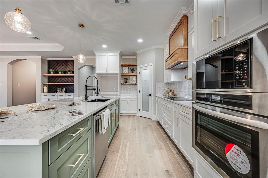 Kitchen with sink, crown molding, hanging light fixtures, a kitchen island with sink, and white cabinets