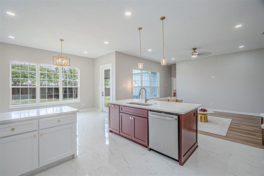 Two tone kitchen featuring stainless steel dishwasher, open floor plan, light stone countertops, hanging lights, and two tone cabinetry