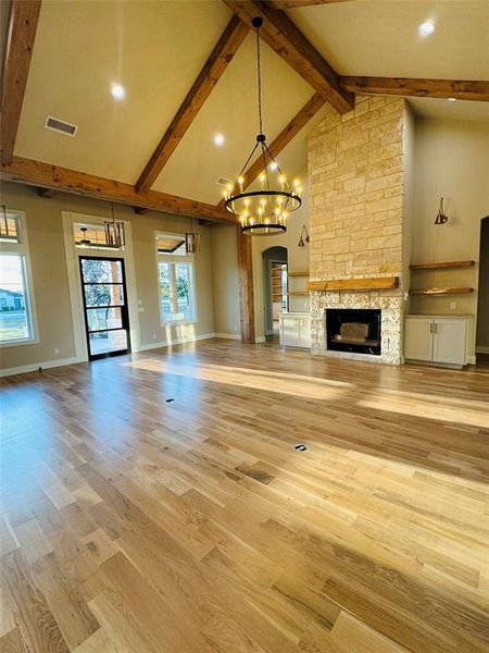 Unfurnished living room with beam ceiling, a notable chandelier, high vaulted ceiling, and light wood-type flooring