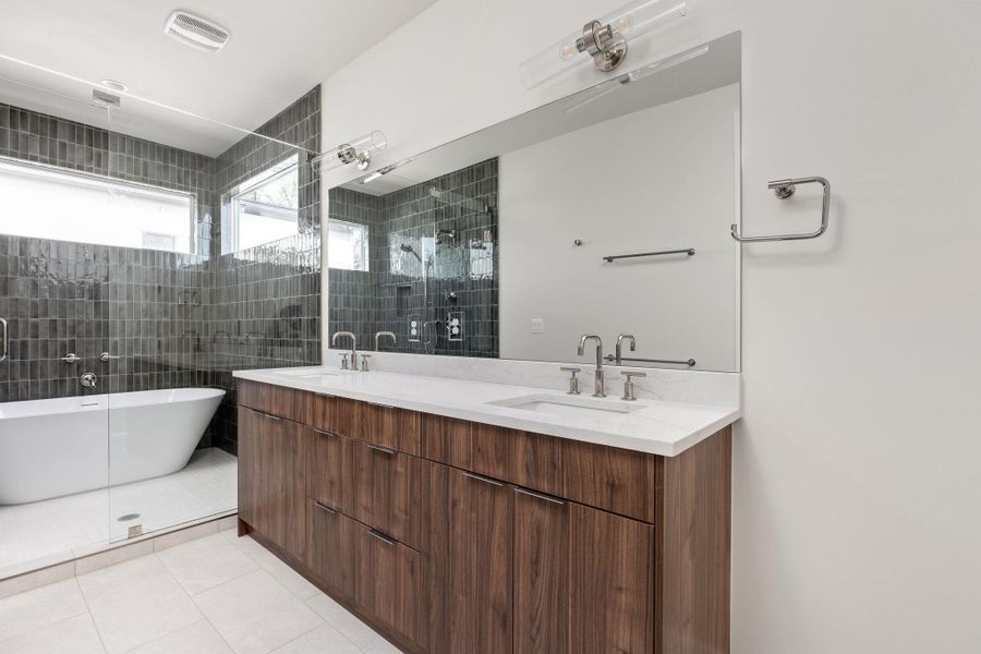 Bathroom with tile patterned flooring, double vanity, tiled shower, and a sink