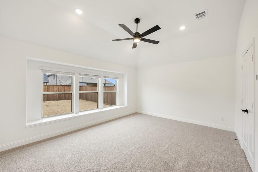 Empty bedroom with carpet flooring, black ceiling fan, and large window overlooking backyard fence Empty bedroom with carpet flooring, black ceiling fan, and large window overlooking backyard fence