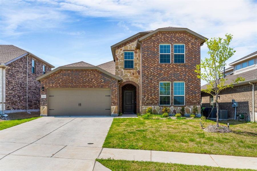 Traditional-style house featuring stone siding, an attached garage, concrete driveway, brick siding, and a front lawn