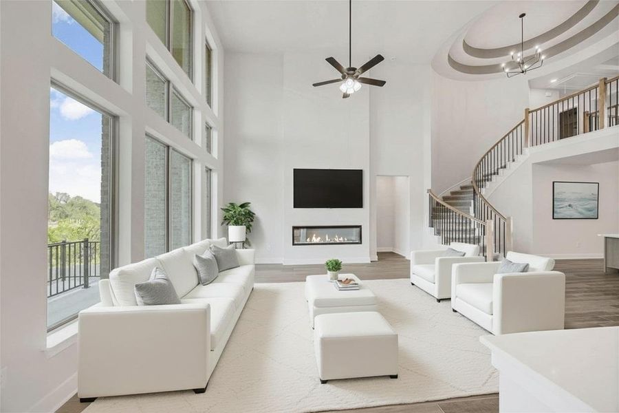 Living area with a fireplace, ceiling fan, a towering ceiling, plenty of natural light, and stairway