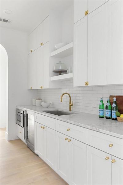 Kitchen with white cabinetry, light hardwood / wood-style flooring, sink, and beverage cooler