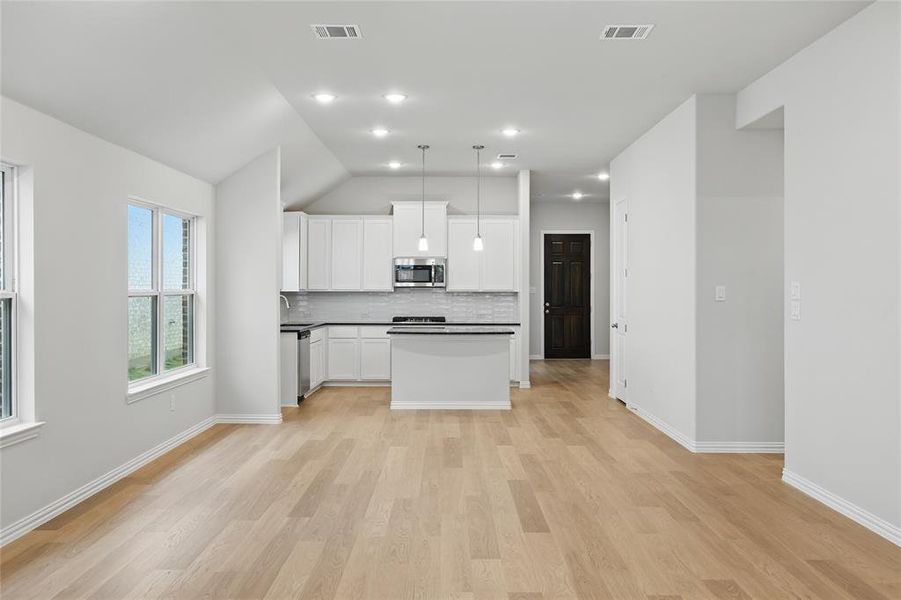 Kitchen featuring white cabinetry, vaulted ceiling, a kitchen island, hanging light fixtures, and light wood-style floors Kitchen featuring white cabinetry, vaulted ceiling, a kitchen island, hanging light fixtures, and light wood-style floors