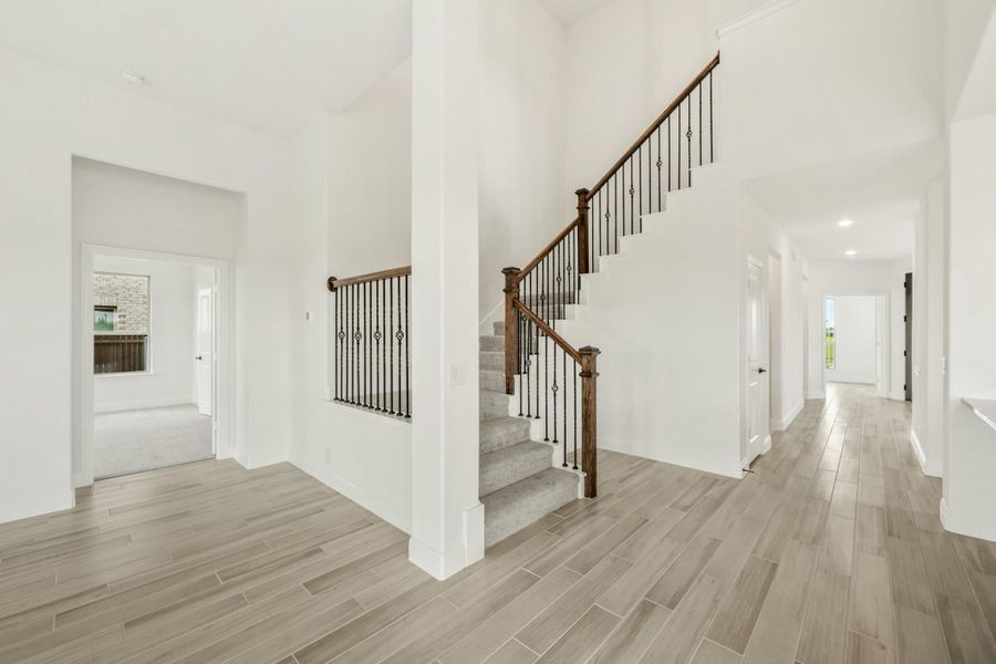 Open foyer with wood-railing staircase, iron balusters, high ceilings, and light wood-look tile floors Open foyer with wood-railing staircase, iron balusters, high ceilings, and light wood-look tile floors