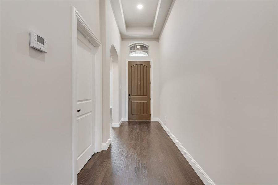 Corridor featuring arched walkways, dark wood-style flooring, a tray ceiling, and a towering ceiling Corridor featuring arched walkways, dark wood-style flooring, a tray ceiling, and a towering ceiling