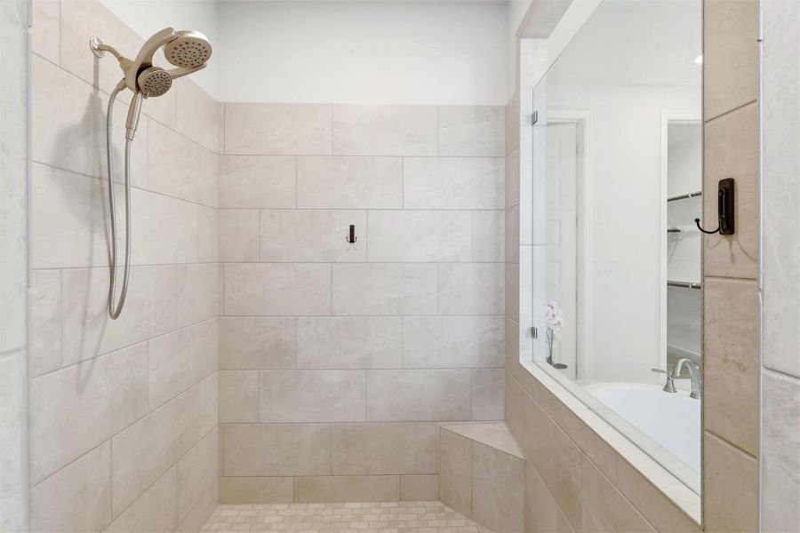 The oversized walk-in shower is beautifully finished with floor-to-ceiling tile, a built-in bench, recessed niche, and large picture window that fills the space with natural light while maintaining privacy.