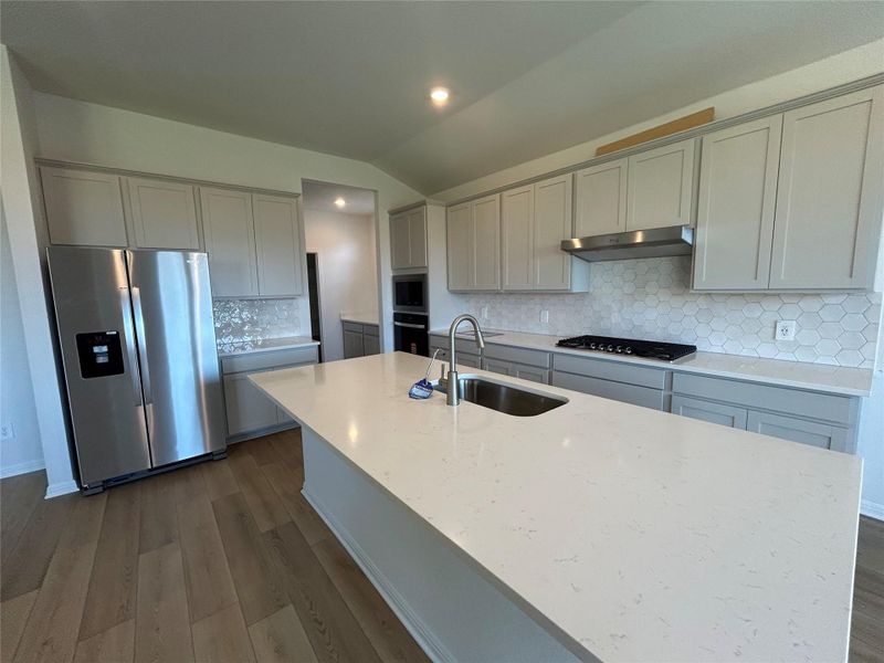 Kitchen with decorative backsplash, stainless steel appliances, gray cabinetry, dark wood-type flooring, and light stone counters Kitchen with decorative backsplash, stainless steel appliances, gray cabinetry, dark wood-type flooring, and light stone counters