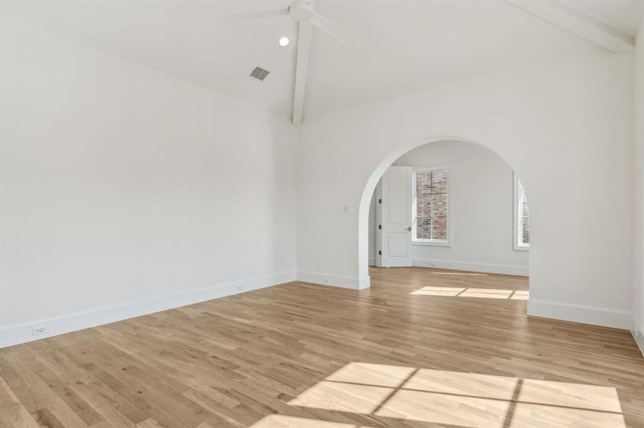 Primary bedroom featuring light hardwood floors, lofted ceiling with beams, and ceiling fan