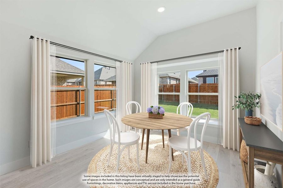Bright dining nook with vaulted ceiling, round wood table, white chairs, and large windows overlooking backyard
