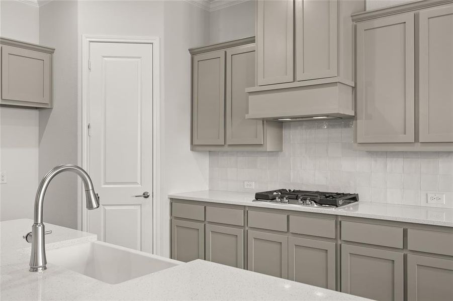 Kitchen featuring gray cabinetry, stainless steel gas stovetop, a sink, ornamental molding, and decorative backsplash Kitchen featuring gray cabinetry, stainless steel gas stovetop, a sink, ornamental molding, and decorative backsplash
