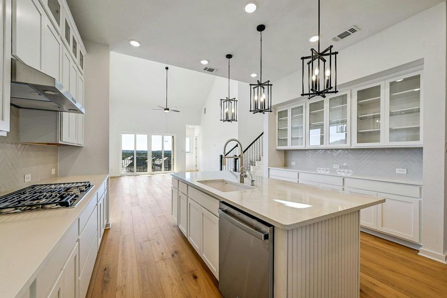 Kitchen with stainless steel appliances, under cabinet range hood, tasteful backsplash, a kitchen island with sink, and a chandelier
