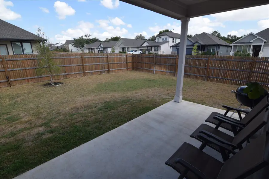 A covered concrete patio overlooks a fully fenced backyard with plenty of lawn space.