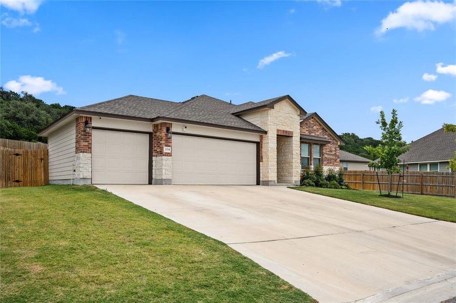 View of front facade featuring brick siding, roof with shingles, an attached garage, concrete driveway, and stone siding