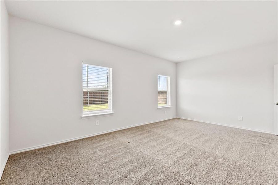 Spacious room featuring neutral carpeting, white walls, two windows with blinds, recessed lighting, and a white door with a silver-tone handle
