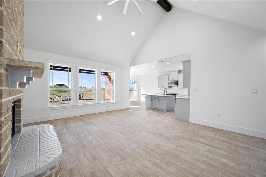 Unfurnished living room featuring light hardwood / wood-style flooring, a fireplace, beam ceiling, and high vaulted ceiling