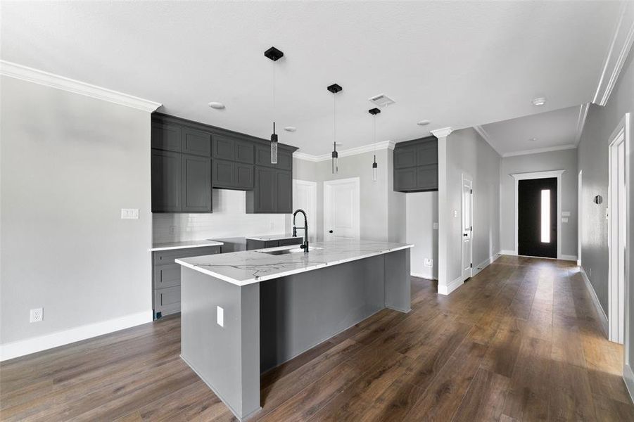 Kitchen featuring light stone counters, crown molding, a kitchen breakfast bar, a center island with sink, and backsplash