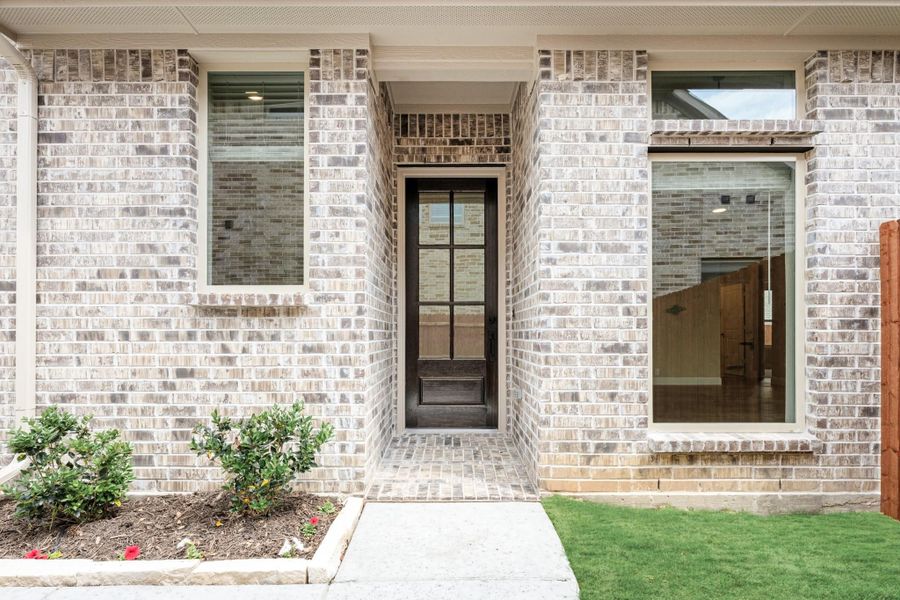 Home entrance with light brick exterior, dark glass front door, and landscaped walkway