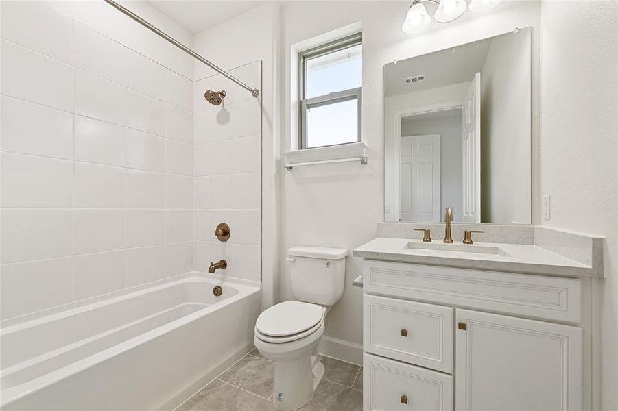 Full bathroom with tile patterned floors, vanity, toilet, and tiled shower / bath combo