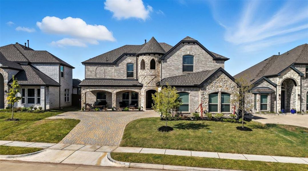 French provincial home with stone siding, a front yard, a porch, and decorative driveway French provincial home with stone siding, a front yard, a porch, and decorative driveway