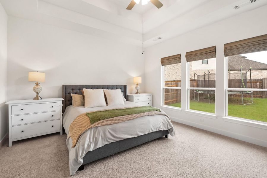 A tranquil bedroom features tray ceilings and ample natural light, creating a serene personal retreat.