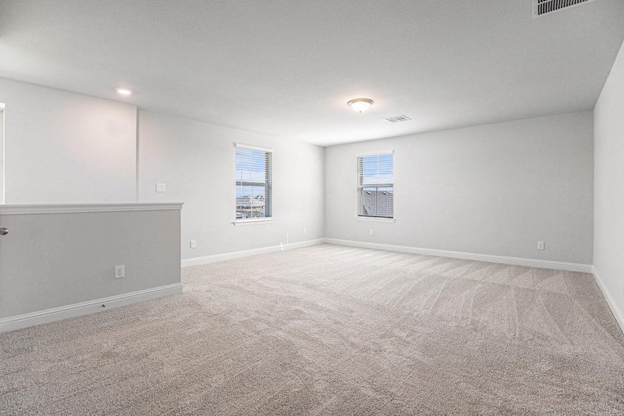 Spacious, bright room with neutral carpeting, freshly painted walls, and ample natural light from two windows. Ideal for a bedroom or living area.