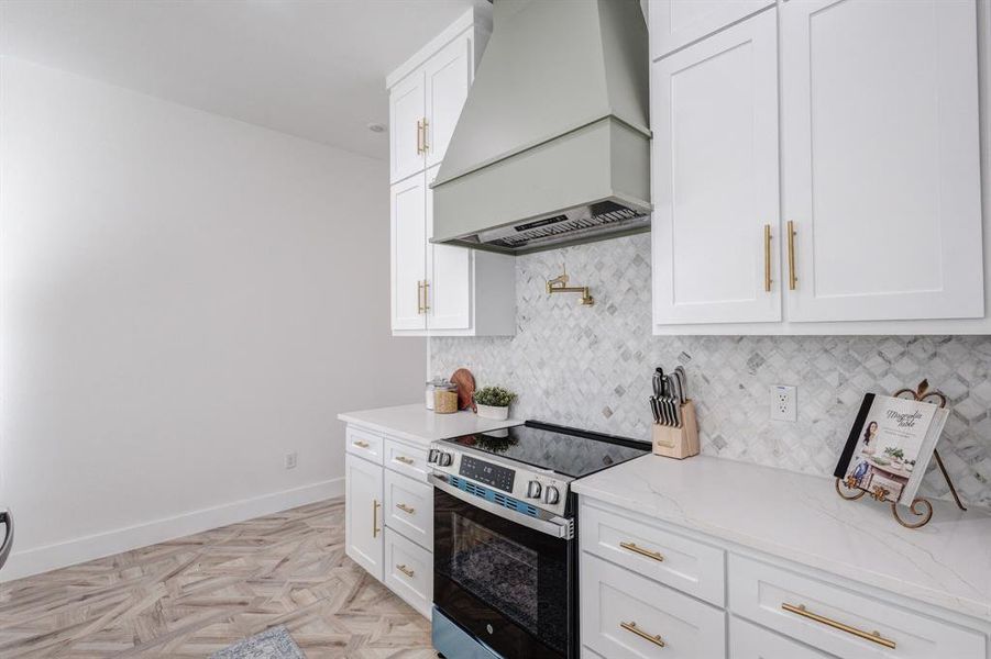 Kitchen featuring premium range hood, stainless steel electric range oven, and white cabinetry