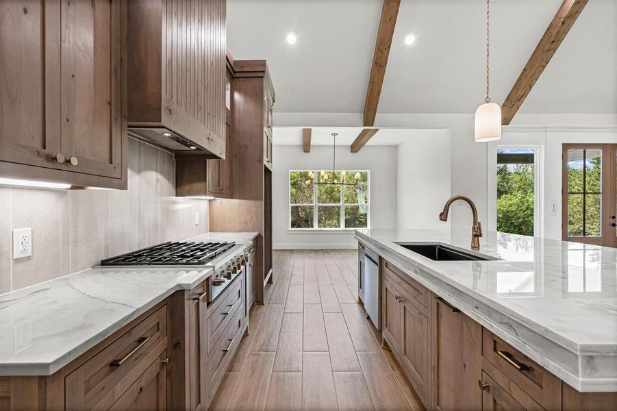 Kitchen with a large island, light stone counters, hanging light fixtures, appliances with stainless steel finishes, and beam ceiling Kitchen with a large island, light stone counters, hanging light fixtures, appliances with stainless steel finishes, and beam ceiling