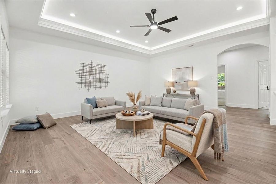 The living area features tray ceilings with recessed lighting, a ceiling fan, and light wood flooring